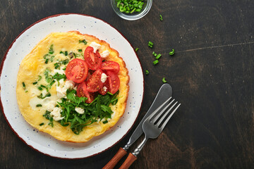 Rustic omelette or frittatas with green onions, cheese mozzarella, green arugula and tomatoes on old wooden dark background. Healthy food concept. Breakfast. Copy space. Top view. Mock up.