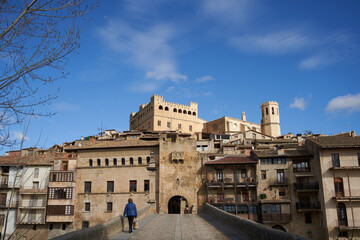 Fototapeta premium A lady with a wicker basket crosses the historic bridge that leads to the medieval small village. Historical complex of Valderrobres in Spain' North.