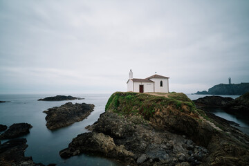 Fototapeta na wymiar White chapel on the rock cliff at sunrise on the Atlantic coast in a cloudy day by the seashore. 
