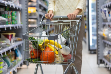 a woman pushes a cart in a supermarket and chooses food and groceries. a European woman in a medical mask. in the grocery store and household chemicals. purchase of goods for adults and children in