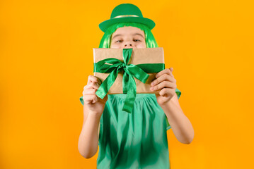 Funny girl with green a hat holds gift on a yellow background. Happy Patrick's Day.