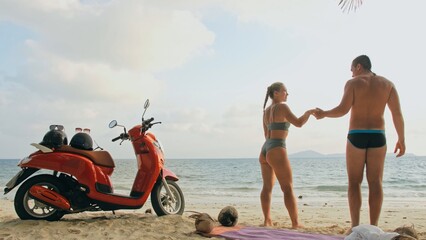 Scooter road trip. Lovely couple on red motorbike in white clothes on sand beach. Wedding just...
