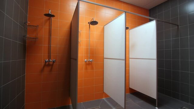 Shower cabins with metal shelves in empty room with bright orange tiles on wall in contemporary sports complex