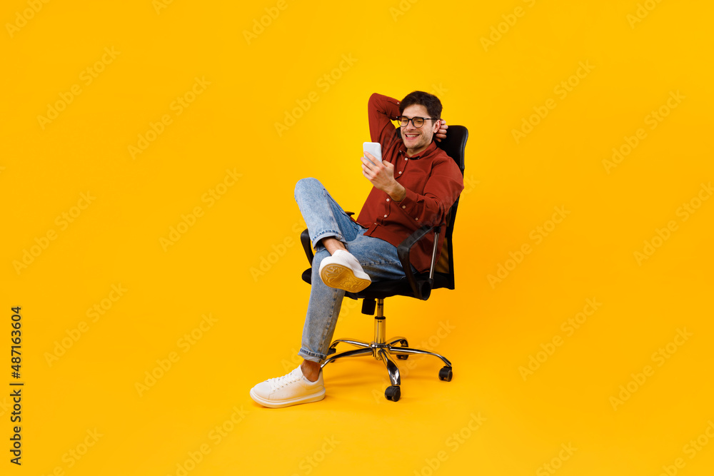 Poster man using smartphone sitting in chair texting over yellow background