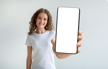 Fototapeta na wymiar Pretty curly young woman holding smartphone with empty screen