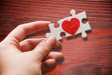 closeup of two pieces of a puzzle forming a heart on a wooden surface,