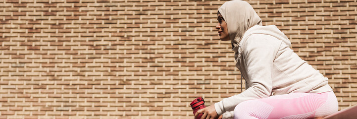 Middle eastern woman in hijab sitting on bench during workout