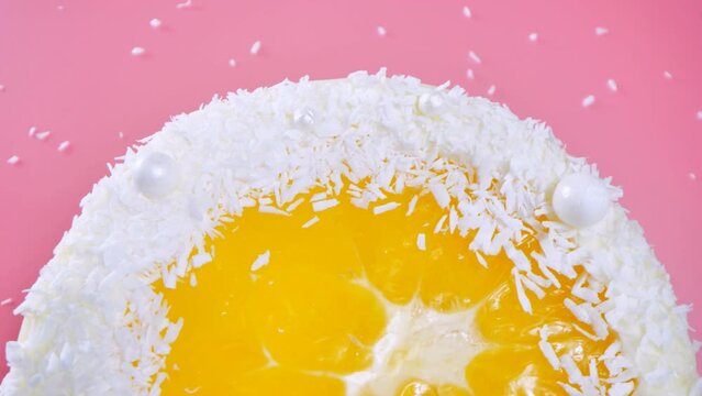 Cake with orange and coconut shavings spun on a pink background.