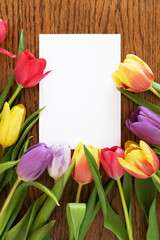 Colorful spring bouquet of tulips on wooden background, white card copy space. Top view, flat lay, mockup for greetings: March 8, Mother's Day, Birthday