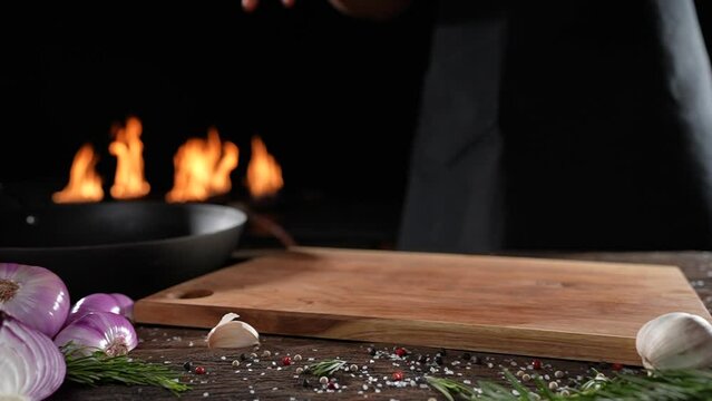 Raw seasoned rib eye steak meat beef dropped on wooden chopping board on a wooden table prepared for cooking with flames in the background. slow motion