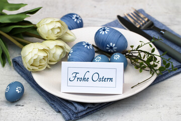 Osterkarte: Gedeckter Ostertisch mit blauen Ostereiern, Teller und Besteck und dem Text Frohe...