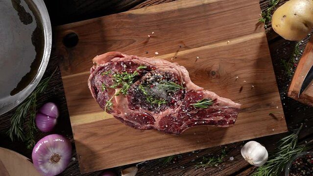 Top view of raw seasoned rib eye steak meat beef dropped on wooden chopping board on a wooden table prepared for cooking. slow motion