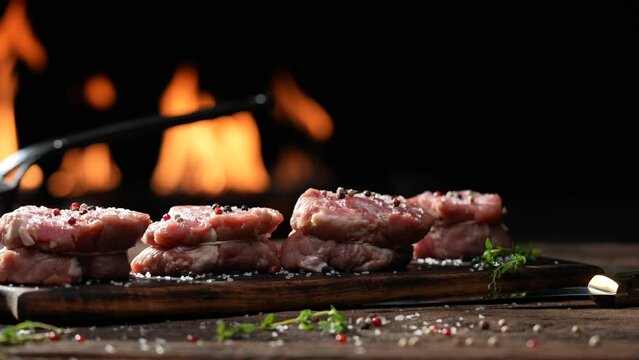 Raw tenderloin steak meat beef sprinkled with salt and seasoning on wooden chopping board on a wooden table prepared for cooking with flames in the background. slow motion