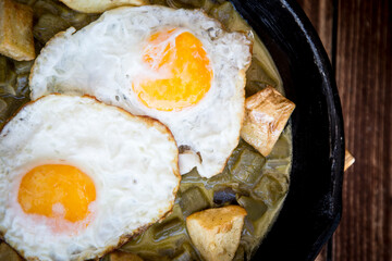 Delicious breakfast with two eggs in green sauce and pan-fried potatoes.
