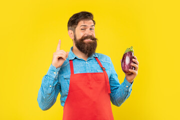Happy man with eggplant in apron got idea keeping finger raised yellow background, shopkeeper