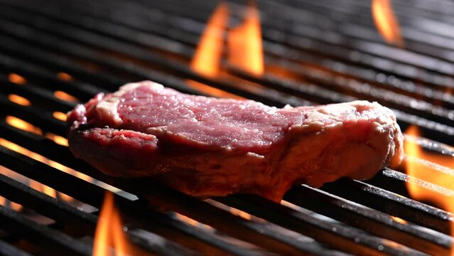 Grilling raw steak meat beef on flaming grill. slow motion