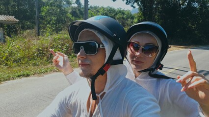Two caucasian tourist woman man drive on red scooter. Make it selfie. Love couple on motorbike in white clothes to go on forest road trail trip. Motorcycle rent safety helmet sunglasses. Ride tourism.