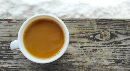 Winter frosty morning, a cup of coffee with milk on a wooden table, snow around