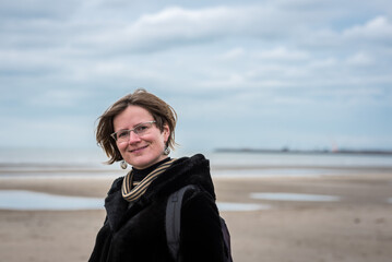 Portrait of a 30 year old white woman, standing on the beach with winter clothes