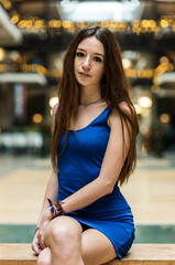 Fashion portrait of an 18 year old red haired pretty girl sitting legs crossed in a short blue dress