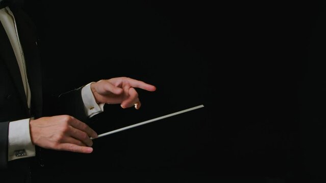 Moving hands of an orchestra conductor directing musicians with movement of baton on black background with lights. Conducting, directing classical musical performance with visible gestures. Close up.