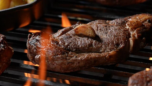 Cooked juicy steak meat beef on a flaming grill surrounded by other meat and sausages. slow motion