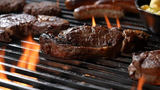 Cooked juicy steak meat beef on a flaming grill surrounded by other meat and sausages. slow motion