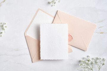 Wedding blank card and pink envelopes with gypsophila flowers on marble table. Flat lay, top view.