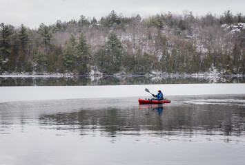 Teen boy paddling a fishing kayak on an icy lake in winter.