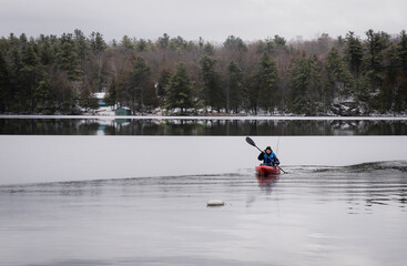 Teen boy paddling a fishing kayak on an icy lake in winter.