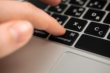 Hand pressing command key on modern laptop keyboard. Command sign and symbol close-up