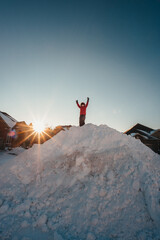 Child in winter jacket climbing big snow pile on a residential street.