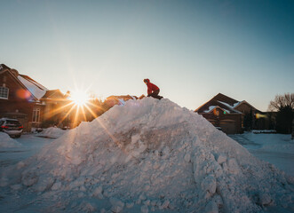 Child in winter jacket climbing big snow pile on a residential street.