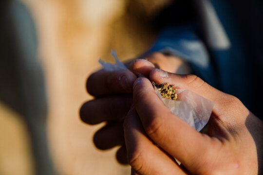 Close-up of a boy's hands rolling a marijuana joint outdoors