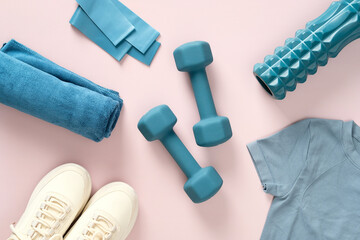 Dumbbells, fitness tape, towel, female sneakers and t-shirt on pink table. Workout equipment top view.