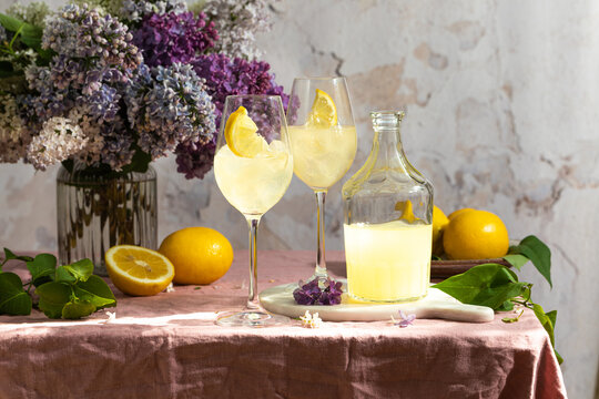 A bottle of Italian traditional liqueur limoncello with glasses, lemons and a vase with blooming lilac