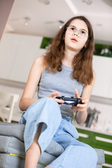 An enthusiastic serious teenage girl is playing with a joystick from a game console in her hands....