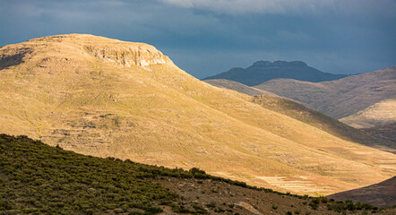 Travel to Lesotho. The sun lights up a mountain as the storm looms