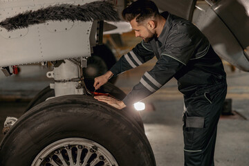 Obraz na płótnie Canvas Bearded man airline maintenance technician repairing airplane landing gear at repair station