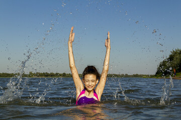 A joyful girl emerged from the sea raising a lot of splashes above her.