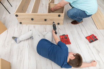 Dad is twisting furniture in the living room and son has fallen asleep on the floor.