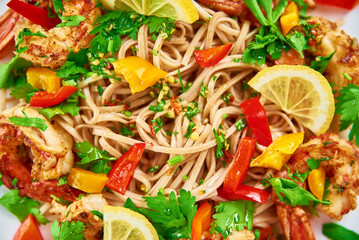 Stir fry noodle with shrimps, lemon and fresh parsley on white plate, soba with prawns, asian cuisine, top view