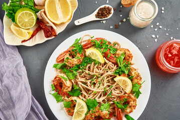 Stir fry noodle with shrimps, lemon and fresh parsley on white plate, soba with prawns, asian cuisine, top view