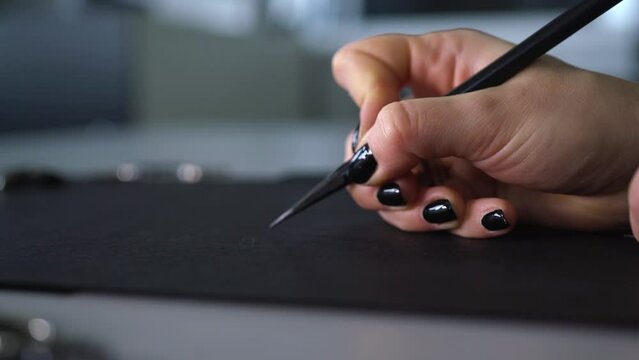 designer artist draws with black pencil on black paper sketch close-up hand