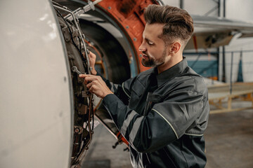 Bearded man maintenance technician tightening bolt with wrench while working at airplane repair...