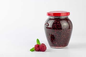 Raspberry jam in glass jar and fresh raspberries on white background.