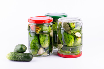 Pickled cucumbers in  glass jar with fresh cucumbers  on white background.