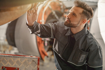 Bearded man maintenance technician using wrench tool while repairing airplane at repair station
