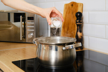 Closeup view of female hand pouring salt to boiling water