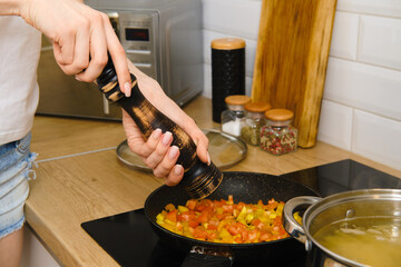 Closeup view of adding black pepper into vegetables in a frying pan